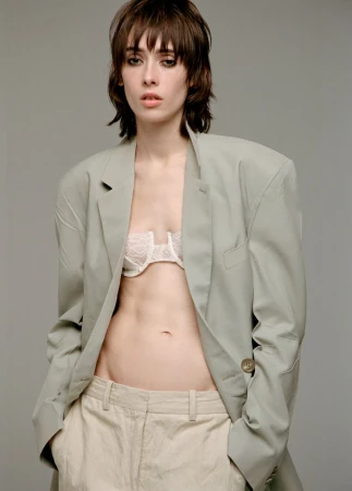Model wearing an oversized sage green blazer and low-rise trousers against a neutral grey studio backdrop.