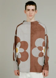 Young man wearing a brown and grey patterned floral long sleeve top against a solid neutral studio backdrop