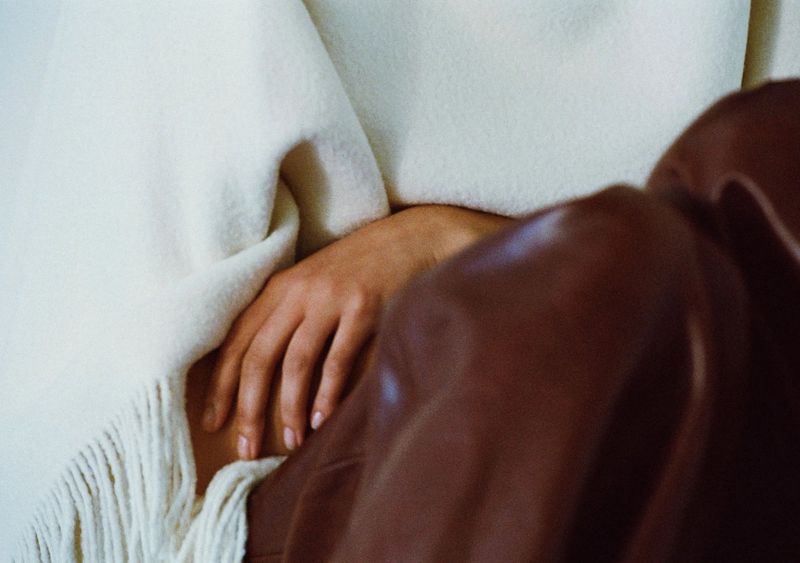 Close-up of a person's hand resting between a cream fringed wool blanket and a dark brown leather jacket.