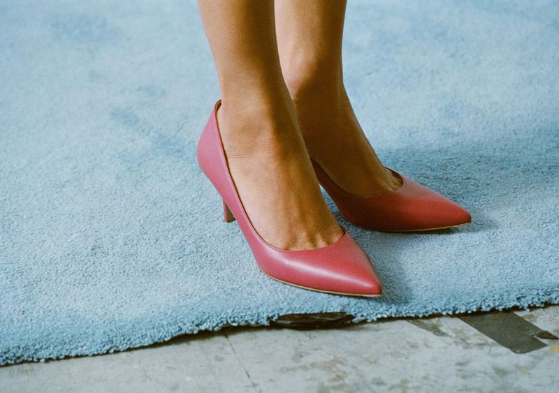 Close-up of a model wearing dusty rose pointed-toe kitten heel pumps while standing on a light blue plush carpet.