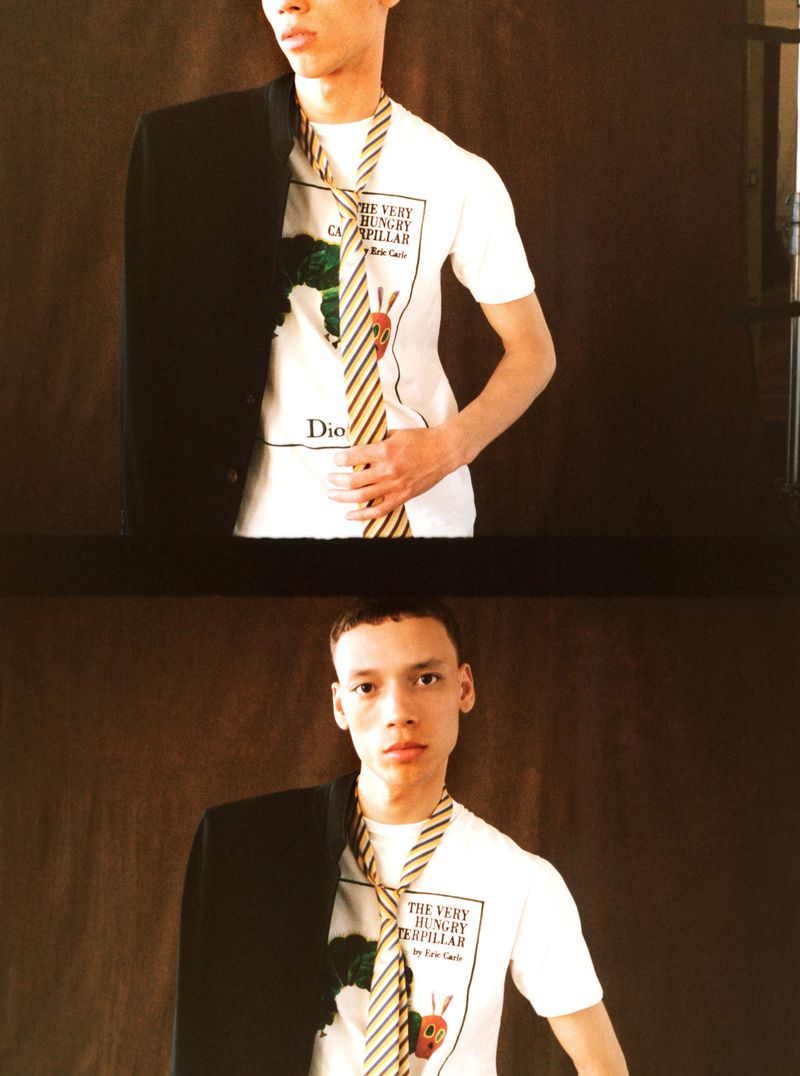 Model Jacoby Sorapuru wearing a graphic white t-shirt and striped tie against a dark backdrop for Jonathan Anderson's Dior.