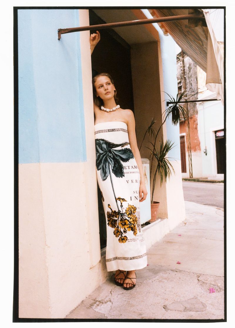 Model Skye Blendermann poses in an open doorway wearing a strapless printed maxi dress with a chunky beaded necklace.