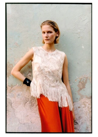 Skye Blendermann posing in a fringe sleeveless knit top and orange skirt against a weathered plaster wall.