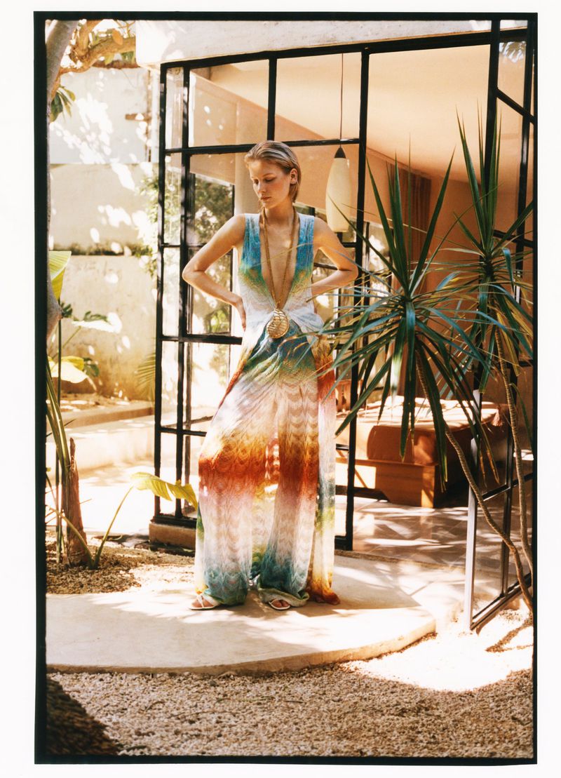 Model Skye Blendermann in a vibrant printed wide-leg halter jumpsuit posing on a sunlit patio for Moda Operandi.