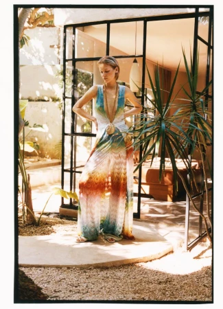 Model Skye Blendermann in a vibrant printed wide-leg halter jumpsuit posing on a sunlit patio for Moda Operandi.