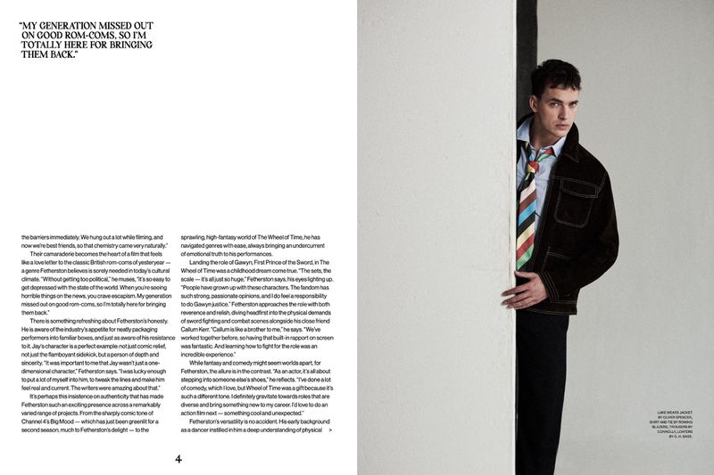 Portrait of a young adult man in dark jacket and colorful tie, looking at the camera and framed by a white wall in a studio setting.