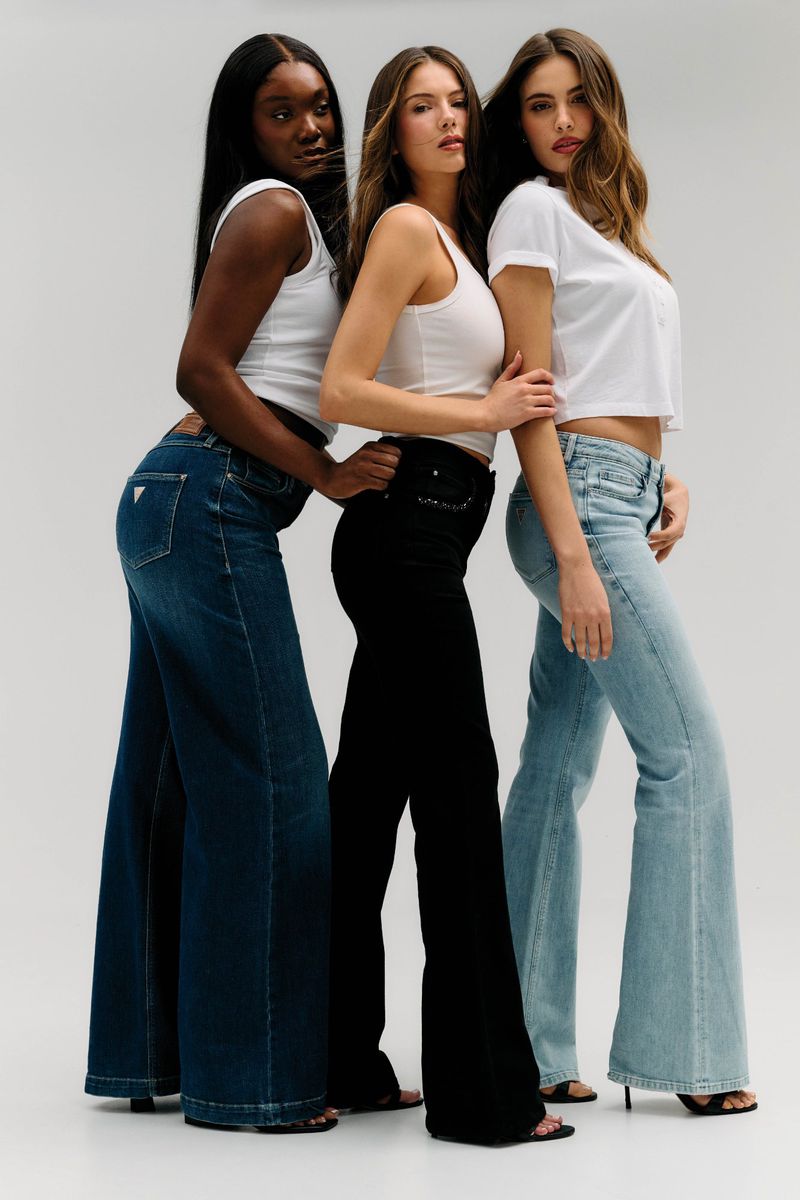 Three female models posing in white tops and flared jeans in different washes against a light studio backdrop.
