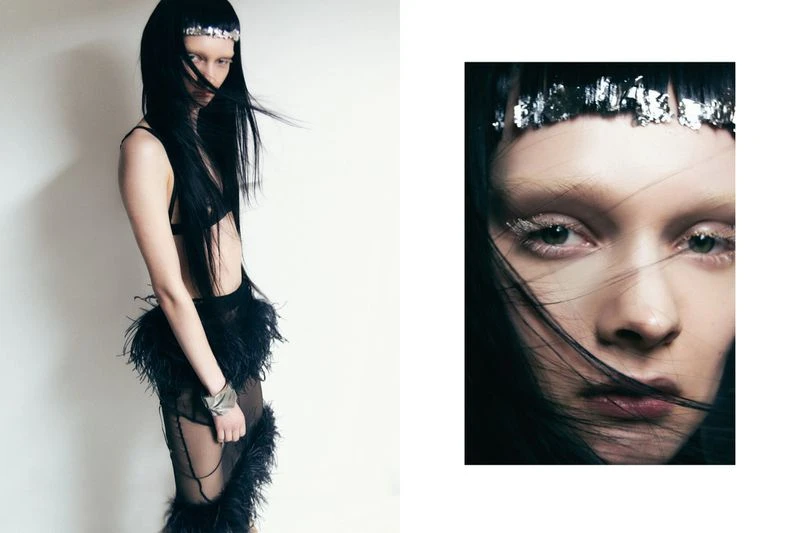 Fashion editorial: Young adult woman with long black hair, silver headband, and black feather trimmed outfit poses in a studio. Close-up detail of face.