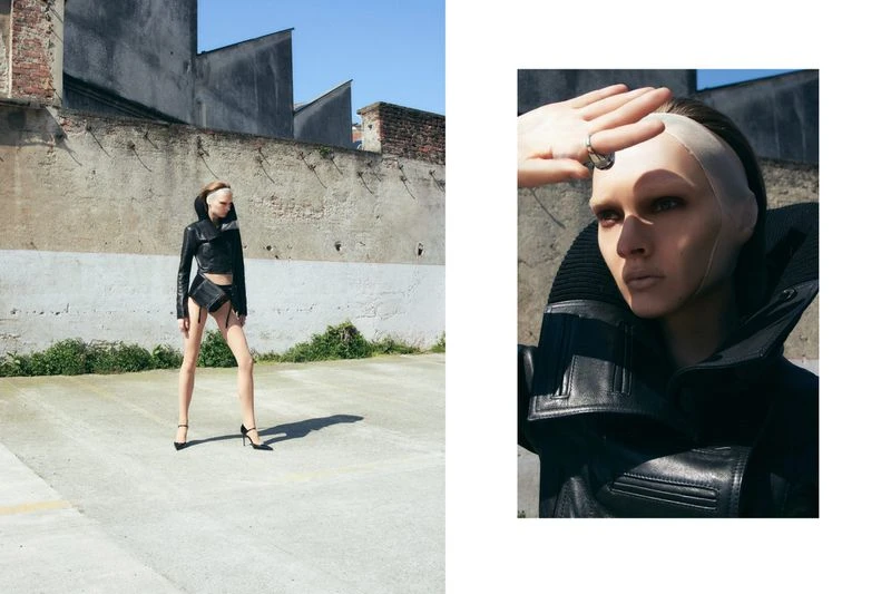 A model in a black leather jacket and high heels poses outdoors against a weathered concrete wall on a sunny day, fashion-forward and edgy.