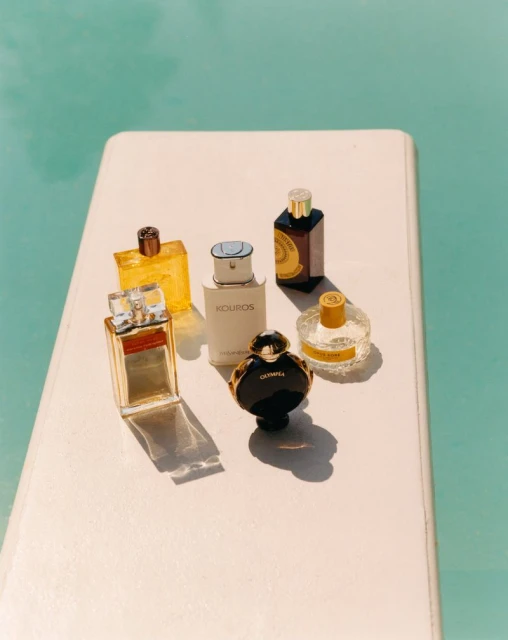 Group of six assorted perfume bottles arranged on a white surface with a turquoise blue background suggesting a pool or water.