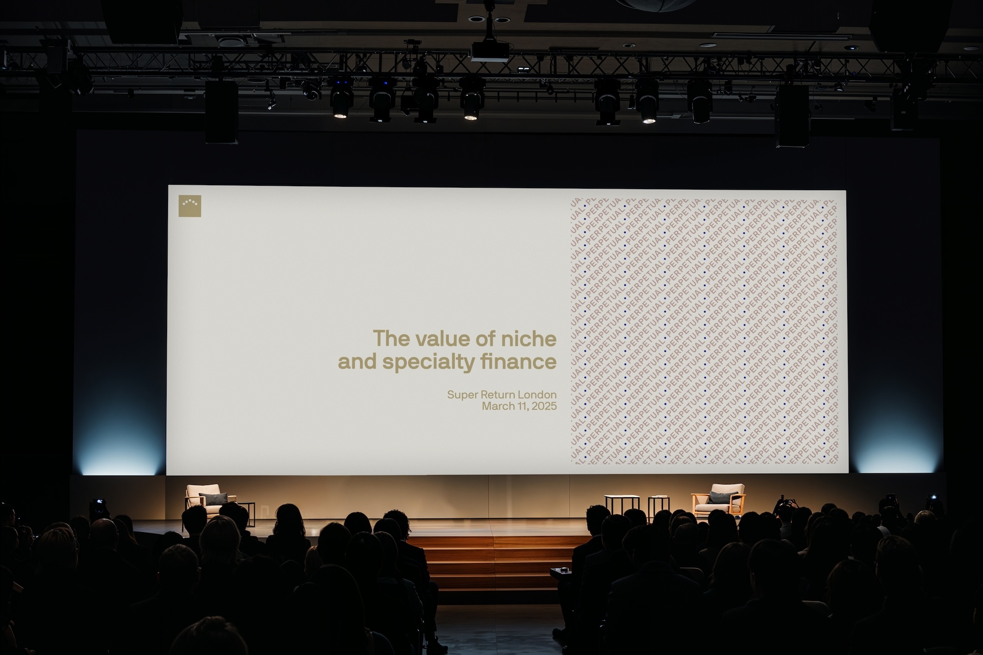 Large presentation screen on an auditorium stage displaying a Perpetual finance keynote slide before a seated audience.