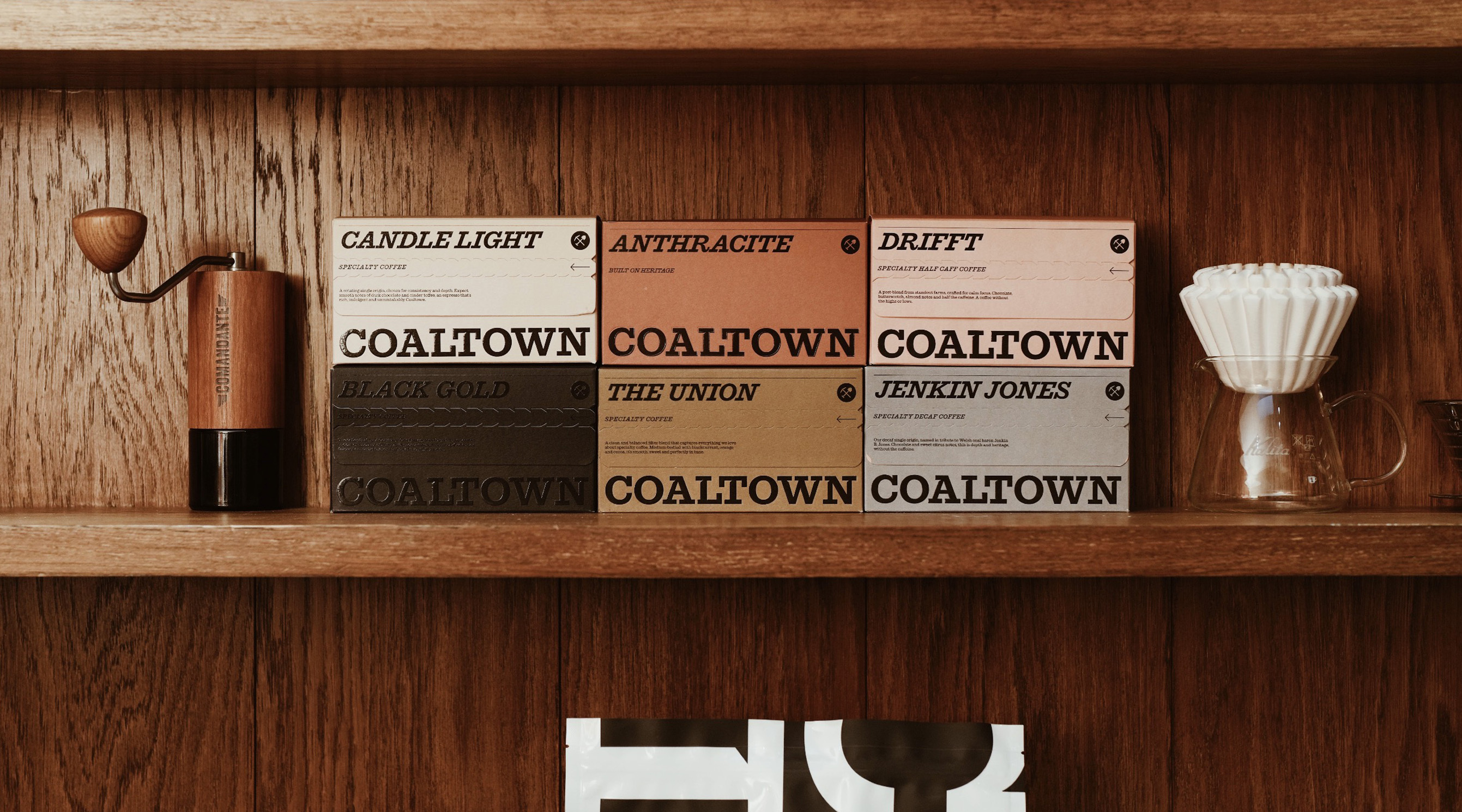 Coaltown Coffee packaging boxes arranged on a wooden shelf alongside a manual hand grinder and a glass pour-over dripper.
