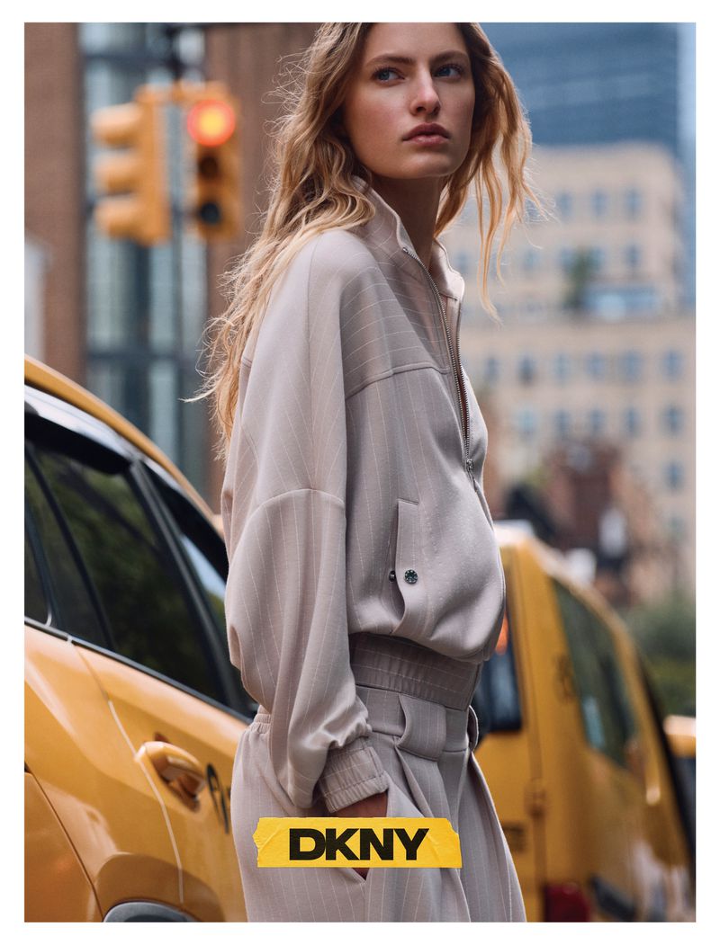 Model Felice Nova Noordhoff posing in a light grey track jacket beside a yellow taxi on a city street.