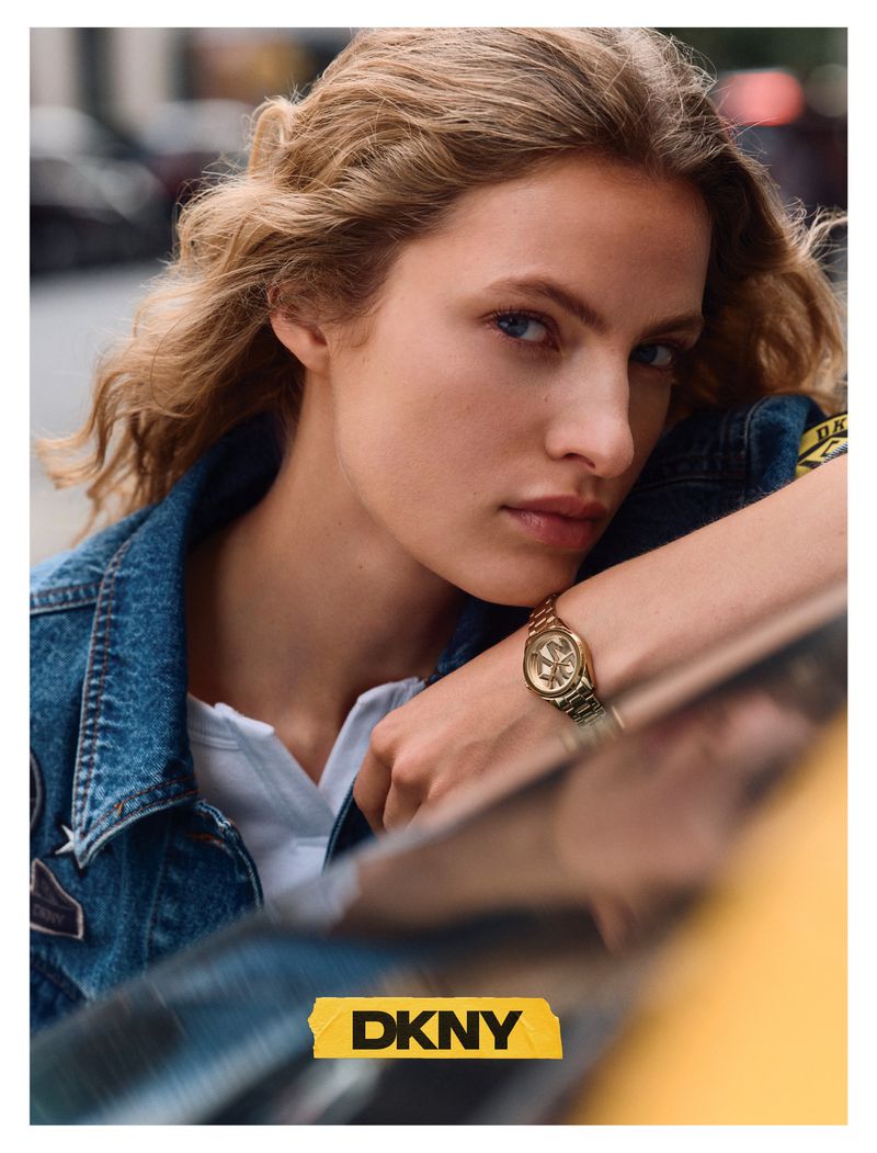Model Felice Nova Noordhoff in a denim jacket and gold watch leaning near a yellow cab in an urban setting.