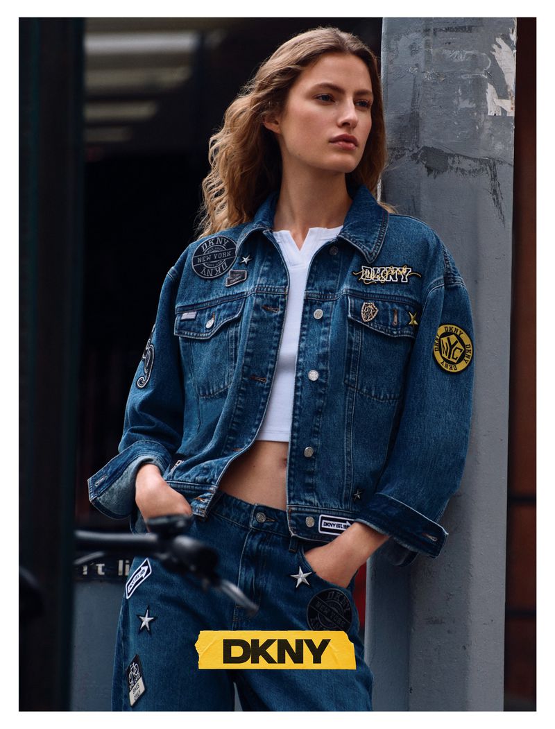 Model in patched denim jacket leaning against a concrete column outdoors
