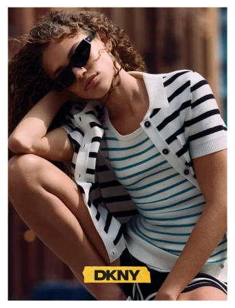 Model wearing black sunglasses and a striped knit short-sleeve cardigan crouching outdoors in sunlight.