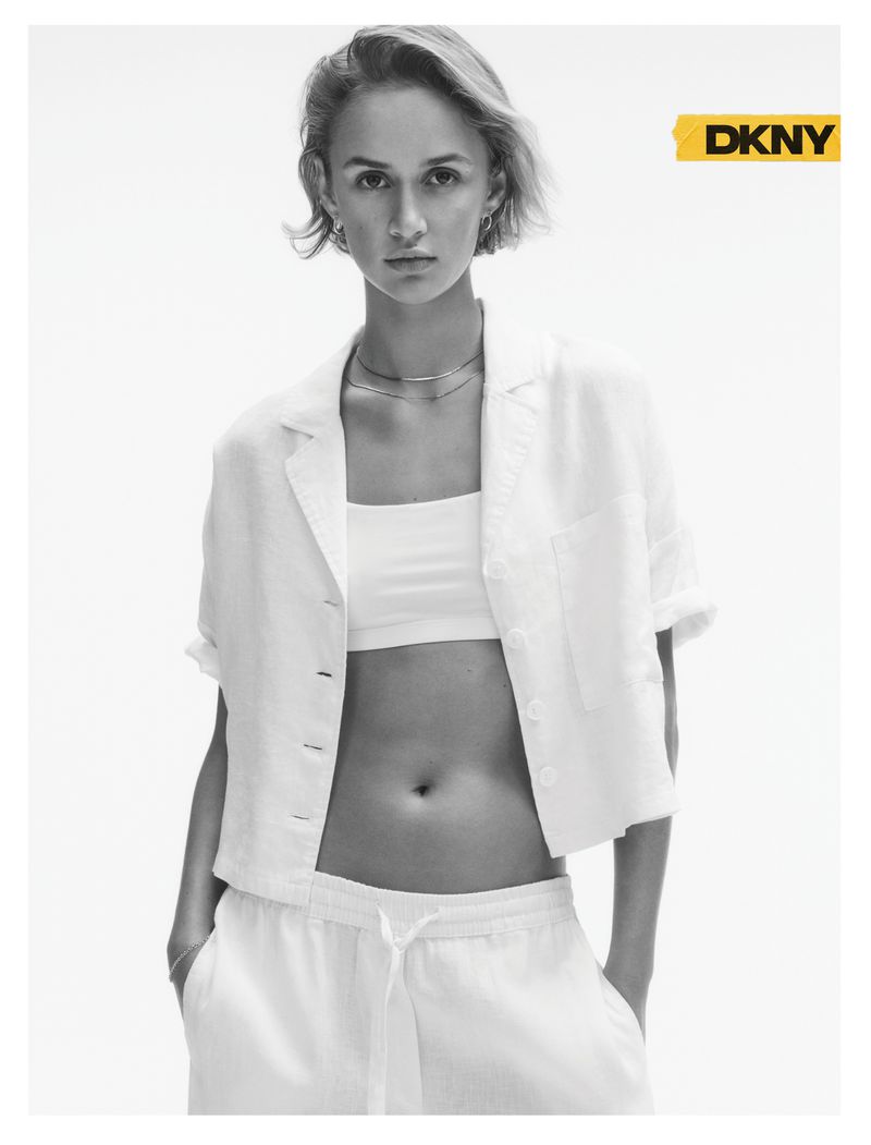Model with short light hair wearing an open white short-sleeve shirt and bandeau top against a white studio background.