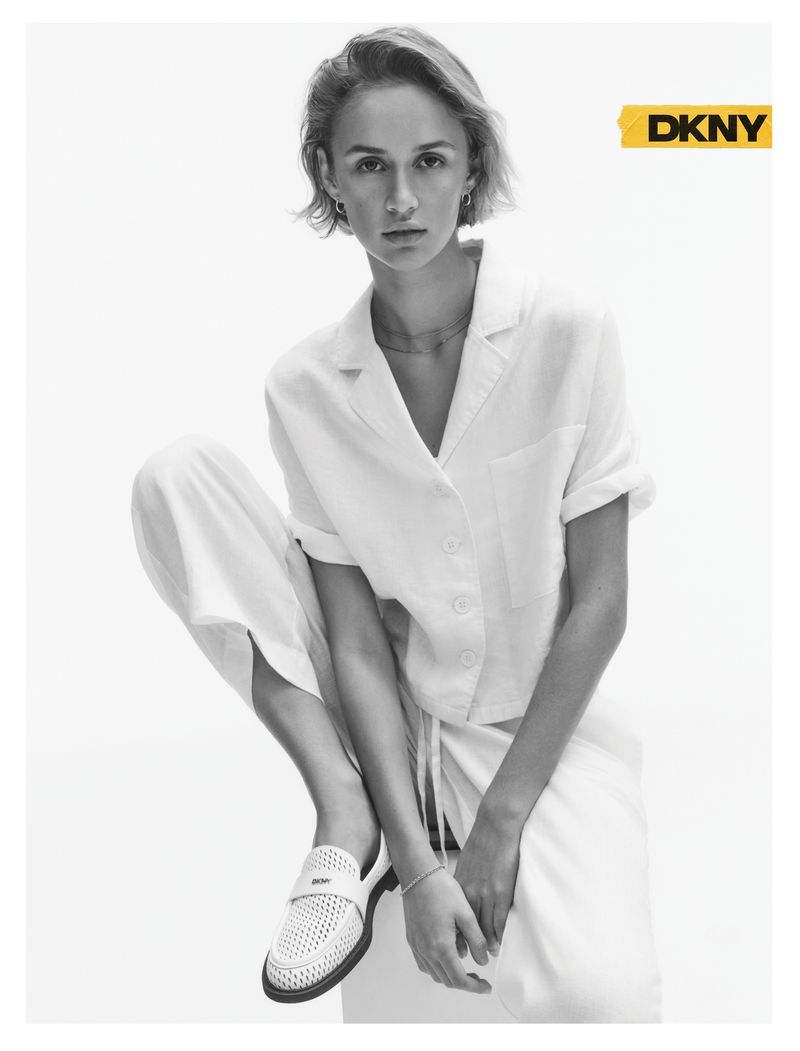 Model Quinn Mora wearing a white short-sleeved buttoned shirt, matching trousers, and white loafers against a white backdrop.