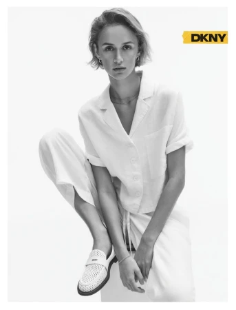 Model Quinn Mora wearing a white short-sleeved buttoned shirt, matching trousers, and white loafers against a white backdrop.