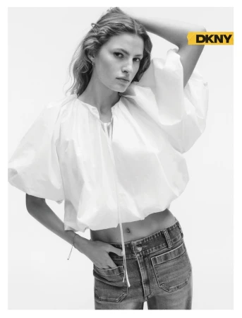 Model Felice Nova Noordhoff in a white puff-sleeve crop top and denim jeans posing against a white studio background for DKNY.