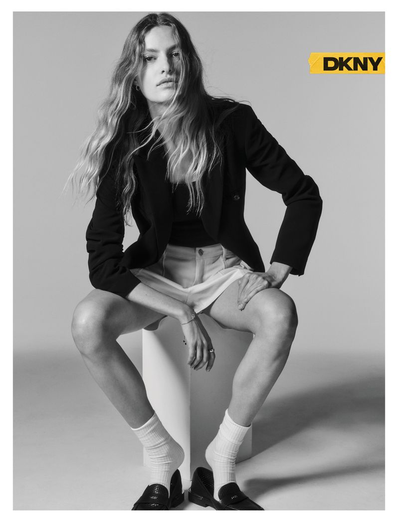 Model Felice Nova Noordhoff seated wearing a black blazer, white shorts, crew socks, and loafers against a studio backdrop.