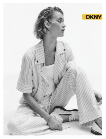 Model Felice Nova Noordhoff seated wearing a striped short-sleeve blazer and matching trousers against a white studio background.