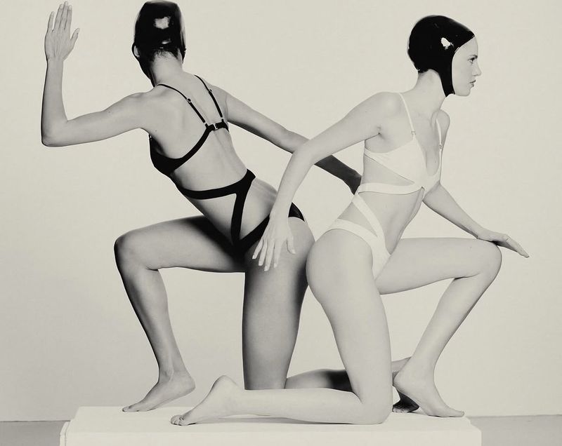 Two models posing in black and white cut-out swimwear and matching swim caps against a clean white backdrop.