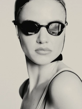 Monochrome portrait of a female swimmer with goggles and a swim cap, captured in a studio setting with soft lighting. The focus is on her face.