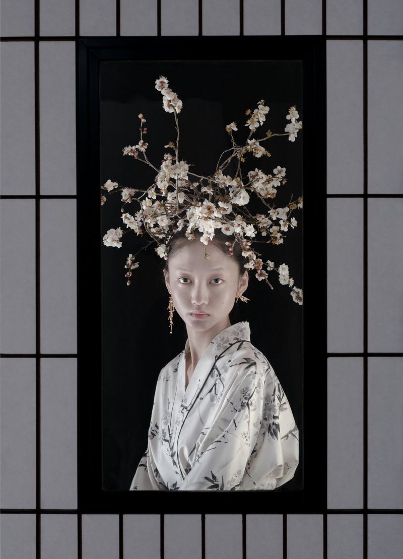 Portrait of a woman in a decorative floral headpiece and floral kimono, framed by a black and white shoji screen.