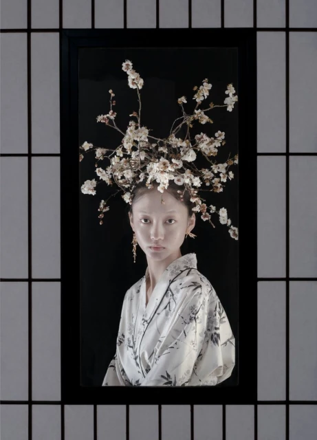 Portrait of a woman in a decorative floral headpiece and floral kimono, framed by a black and white shoji screen.