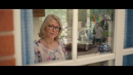 Elderly woman looking out a window wearing glasses and a floral patterned top with color grading by Kali Bateman