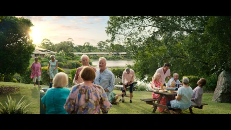 Group of older adults gathered outdoors in a park setting near a lake during sunset for the AVEO TVC project.