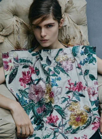 Model Anna Robinson seated in a tufted fabric chair wearing a floral embroidered top for Elle U.S.