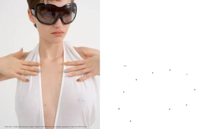 Model Greta Hofer wearing oversized black visor sunglasses and a plunging white halter garment against a clean white background.