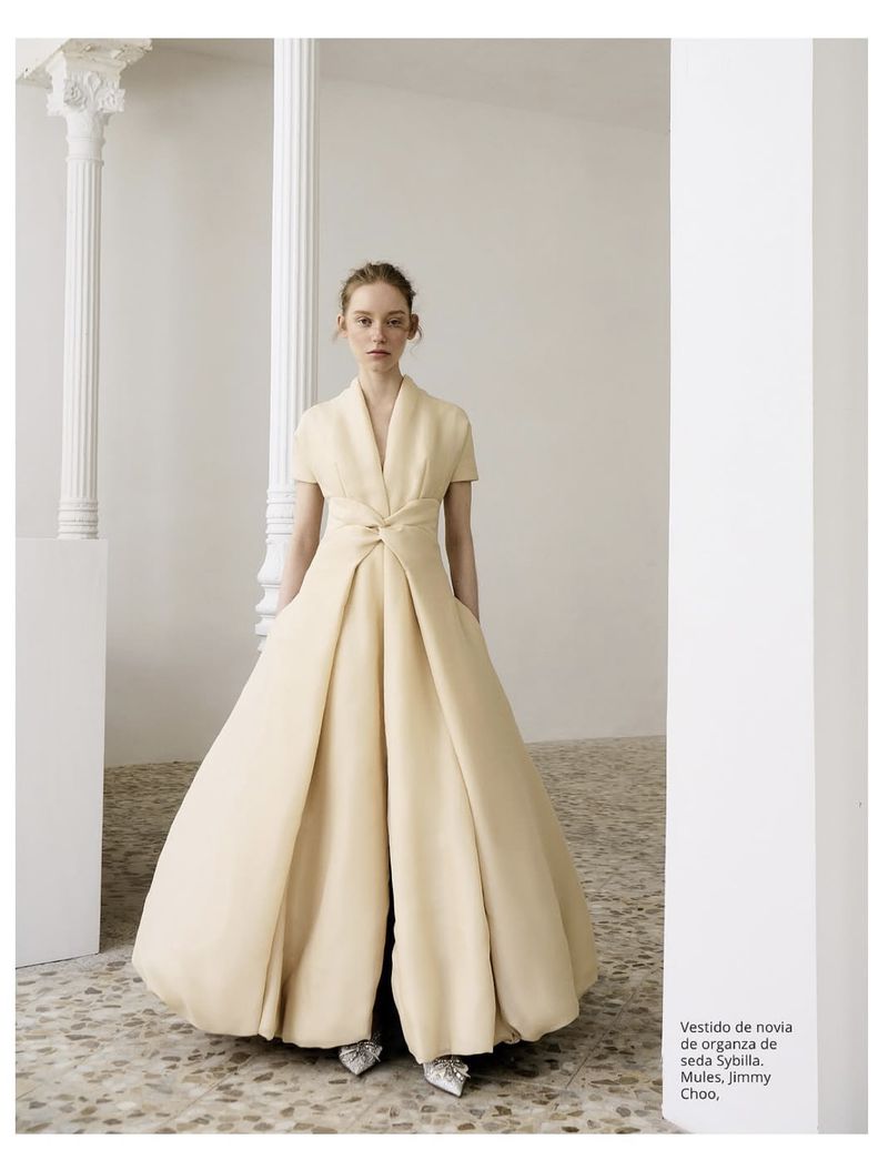 Model Jeske van der Pal wearing a voluminous cream silk organza gown standing on a terrazzo floor between white columns.