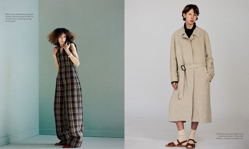 Fashion editorial shot featuring two female models in a studio setting. One model wears a plaid jumpsuit, while the other wears a tan trench coat.