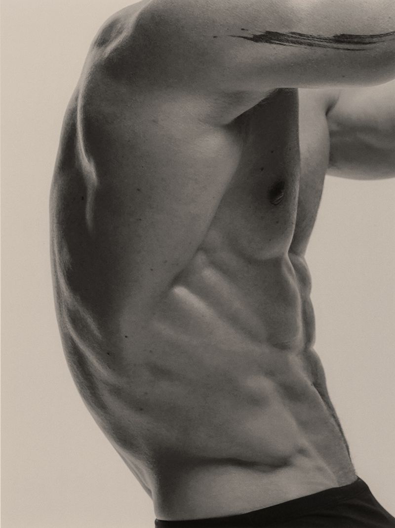 Close-up profile of a muscular male torso and side abdominals against a neutral studio backdrop.