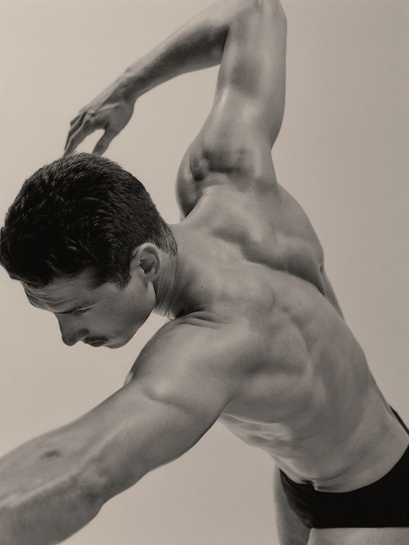 Muscular man posing athletically with arms raised against a plain light background