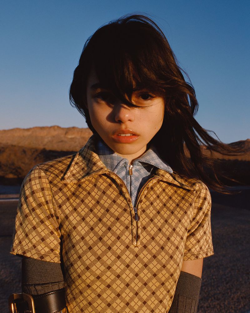 Model in a yellow patterned zip polo shirt and blue collar against an outdoor landscape background