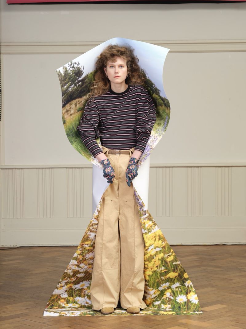 Model Julie Hoomans poses wrapped in a large printed landscape paper backdrop wearing a striped top and wide-leg beige trousers.