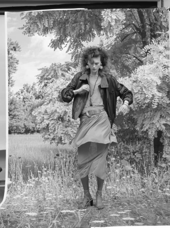 Model Julie Hoomans poses in a leather jacket and draped skirt in front of a printed landscape backdrop in black and white.
