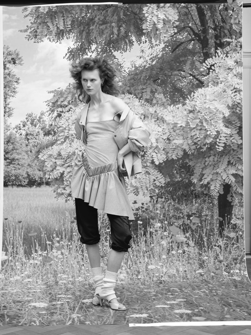 Model Julie Hoomans posing in a drop-waist tunic dress and leg warmers against a scenic monochrome printed backdrop.