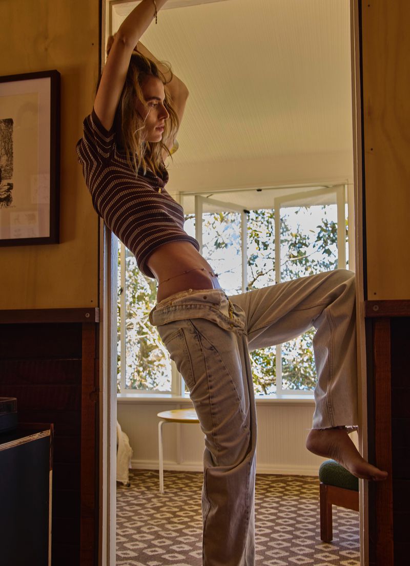 Model Marie-Violaine Chenal posing in a doorway wearing a striped crop top and light-wash denim trousers.