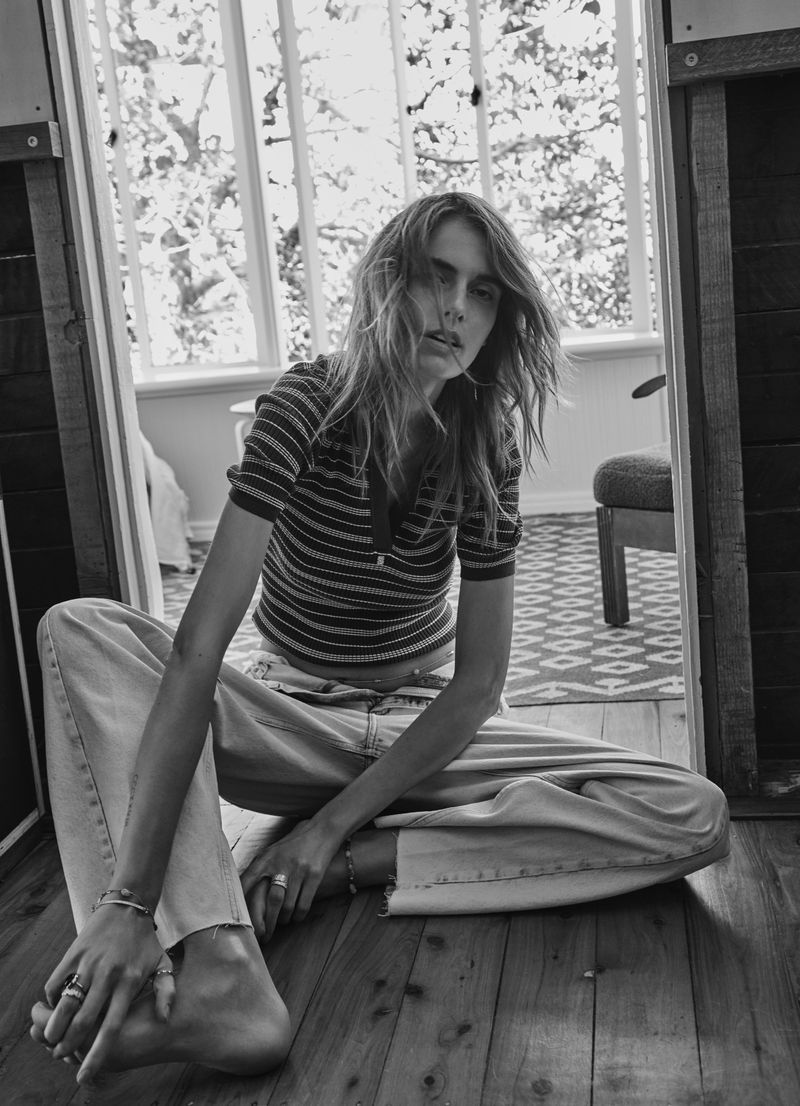 Model Marie-Violaine Chenal seated barefoot on a wooden floor wearing a striped top and wide-leg jeans in black and white.