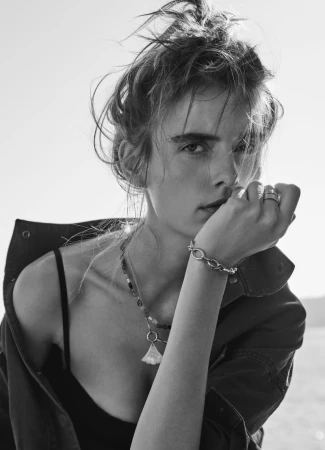 Black and white portrait of model Marie-Violaine Chenal wearing an open shirt and silver jewelry with her hand to her chin.
