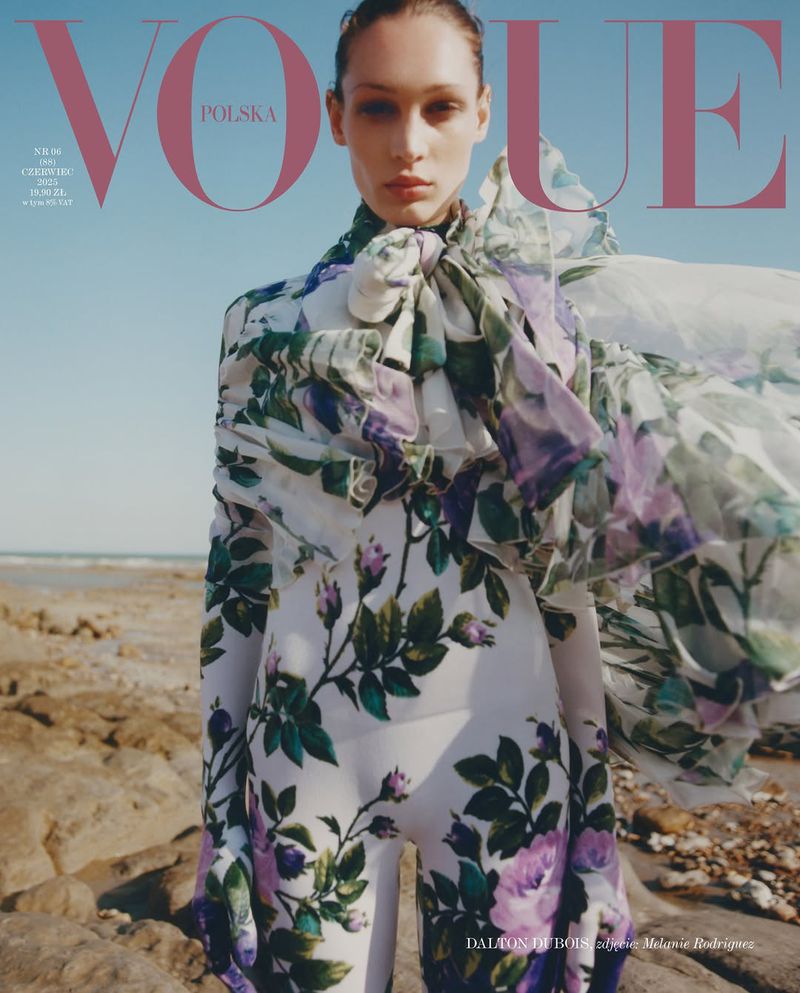 Vogue Polska cover featuring a woman in a floral patterned outfit standing on a beach with tan sand and a clear blue sky.