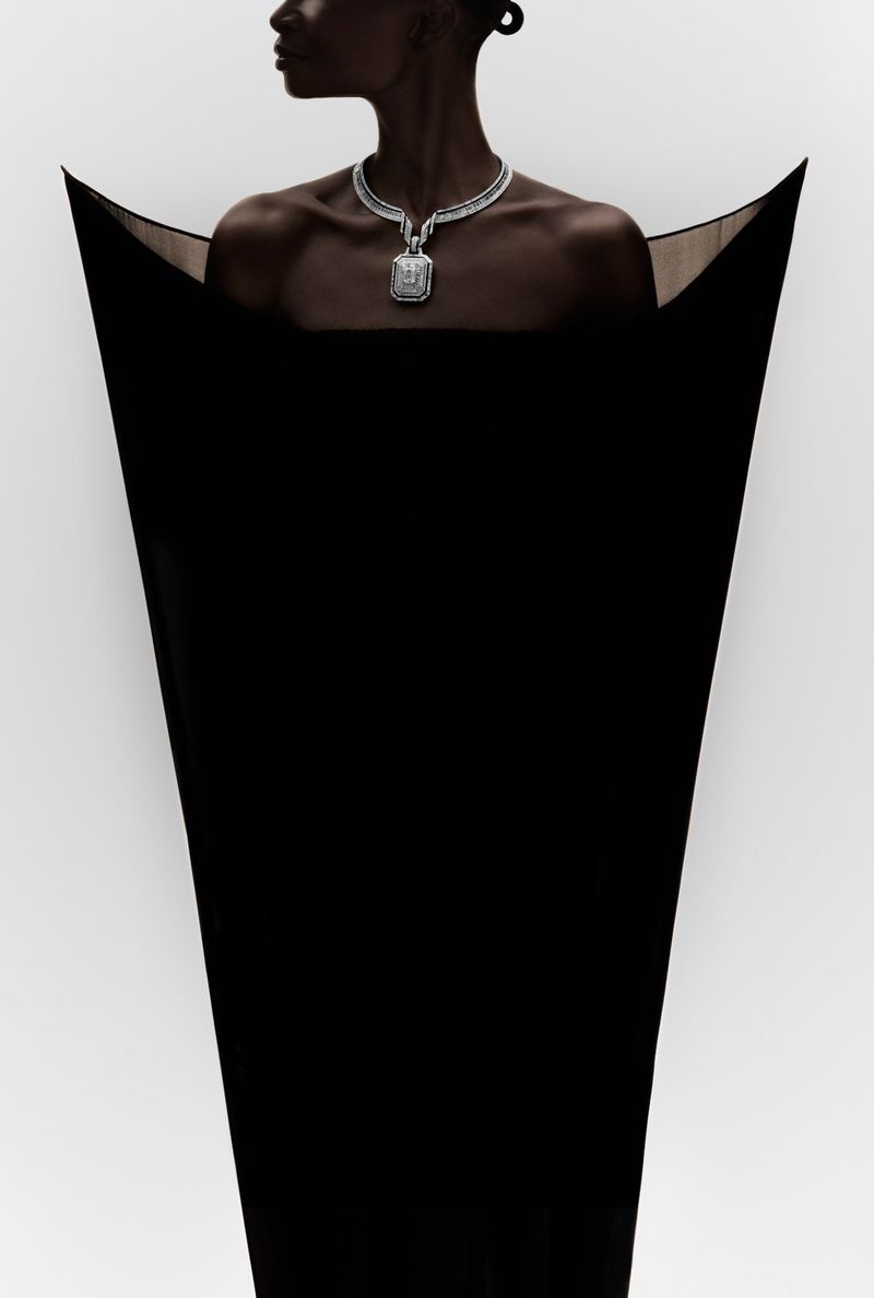 Model Debra Shaw wears a diamond necklace with an angular black sculptural gown against a white background.