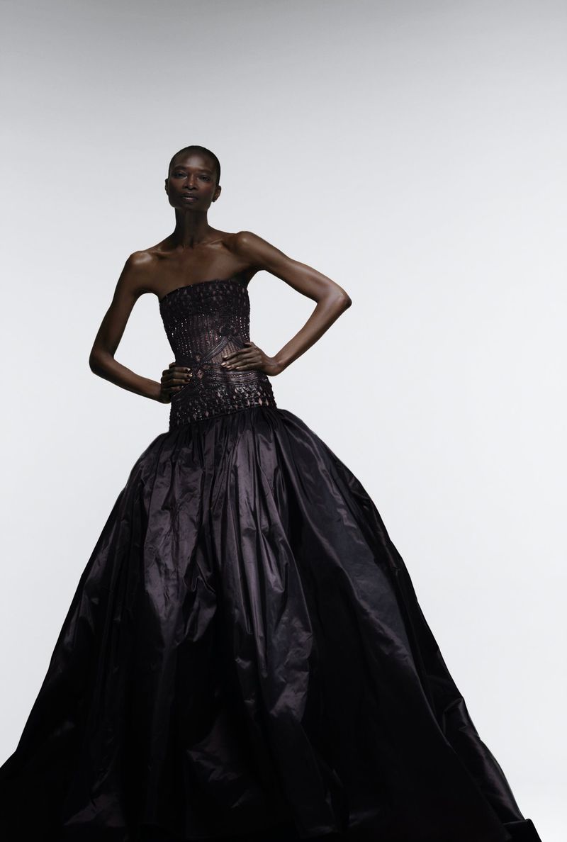 Elegant African American woman in black strapless gown with beaded bodice posing in a studio with hands on hips, beauty and fashion.