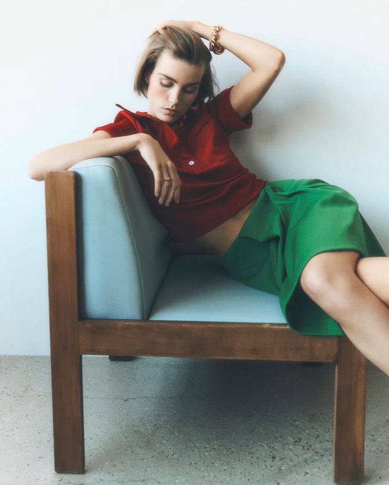 Model Luna Bijl wearing a red top and green skirt seated in a blue armchair for Elle France editorial project Rayons De Couleurs