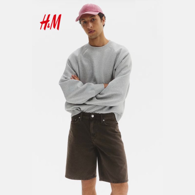 Model Anass Bouazzaoui posing in a grey sweatshirt, washed dark denim shorts, and a pink cap against a white background for H&M.
